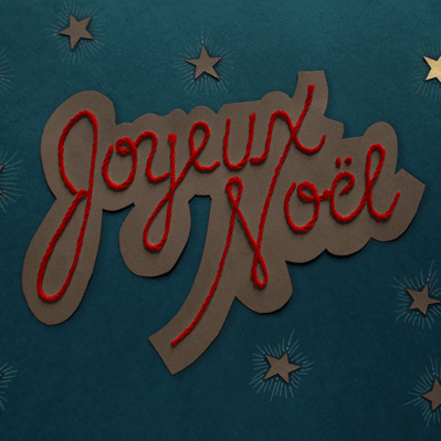 Animated neon of the phrase “Joyeux Noel” in script composed with paper and string, with flashing stars.