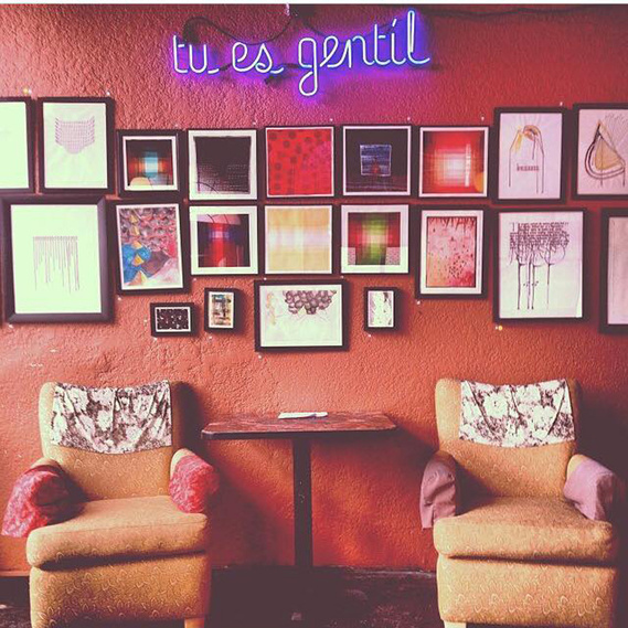 A muted orange colored wall is hung with a couple dozen paintings and the 