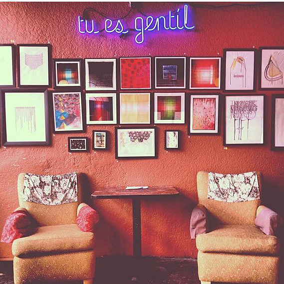 A muted orange colored wall is hung with a couple dozen paintings and the 