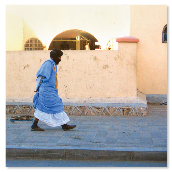 Back cover of the album for Hassaniya Music from the Western Sahara and Mauritania LP, featuring a solitary man wearing a black keffiyeh and blue Deraa walking along a colorful street.