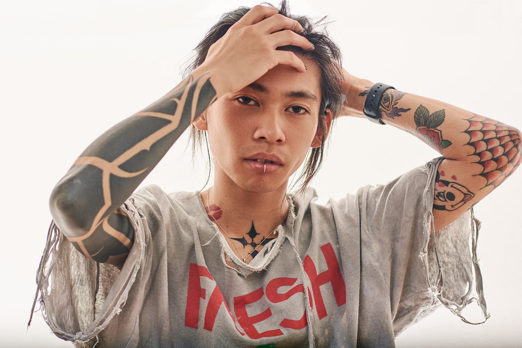 Portrait of a Japanese man with tattooed arms and his hands on his head.