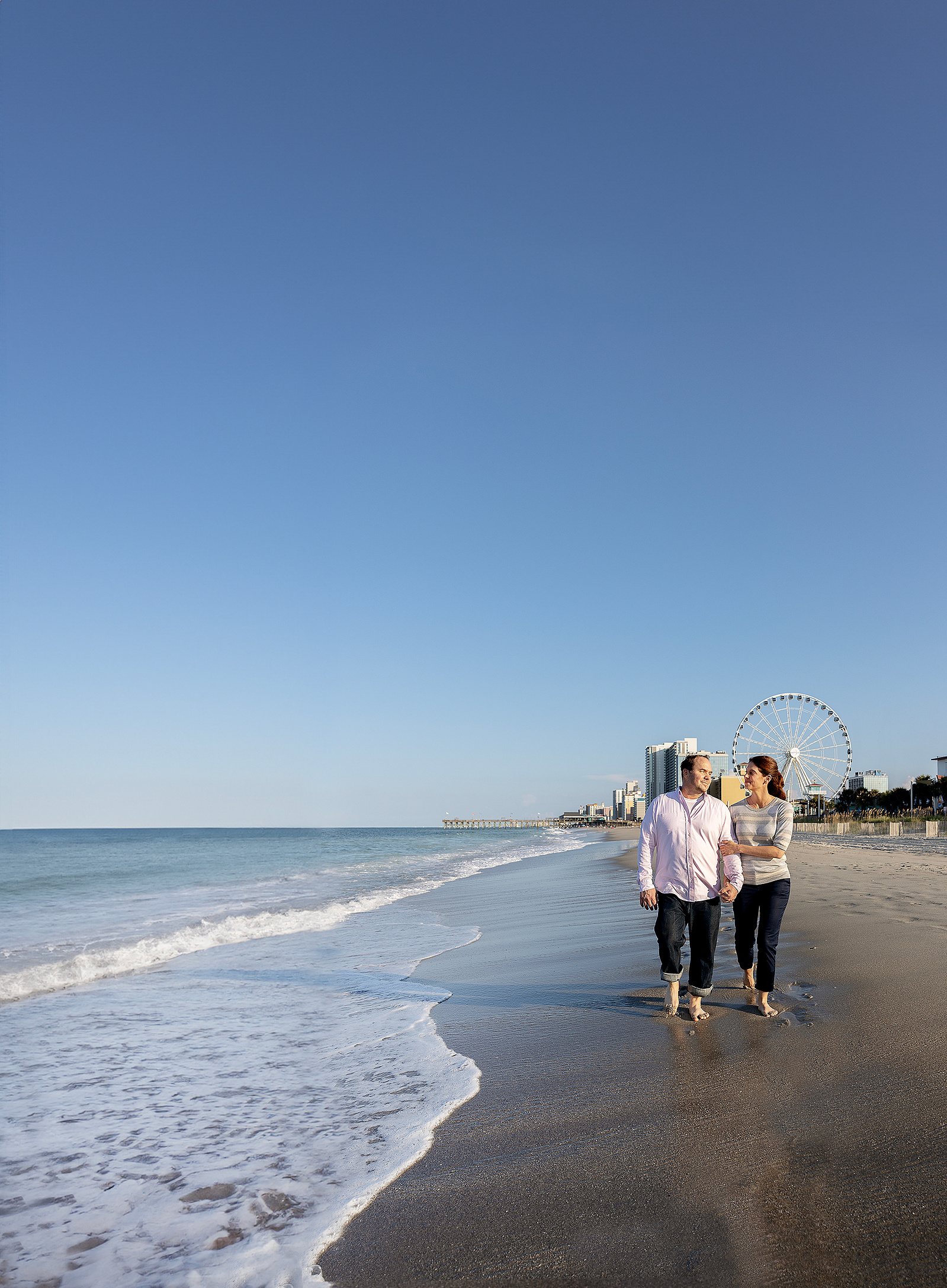 Couple walking on the beach in Myrtle Beach South Carolina with the Sky Wheel in the background on a sunny day.