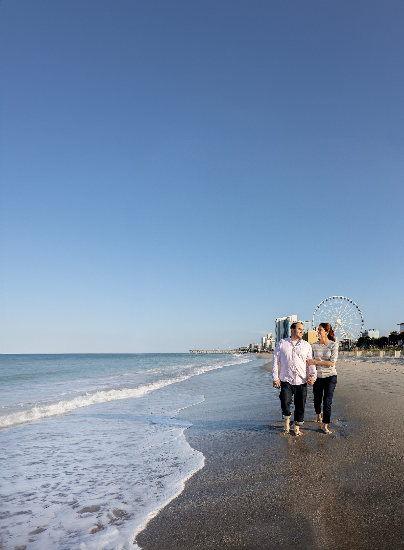 Couple walking on the beach in Myrtle Beach South Carolina with the Sky Wheel in the background on a sunny day.