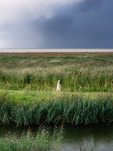 Woman in white, walking in the Estonian prairie, threatening sky. 
Femme en blanc, marchant dans la prairie estonienne, ciel menaçant.