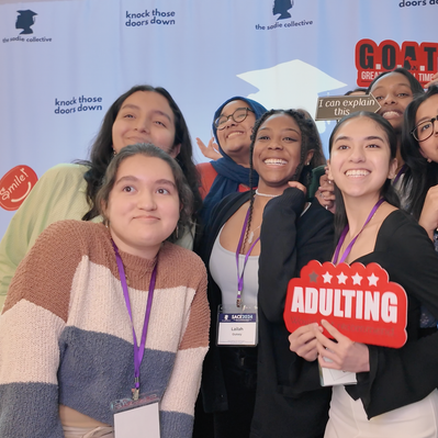 A group of diverse women posing happily in front of a photo booth at The Sadie Collective Event 2024