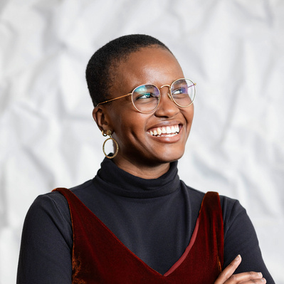 A corporate headshot of a smiling black woman with a buzzed haircut wearing gold-framed glasses, gold earrings, a black turtleneck, and a red velvet tank top at the Kennedy Center in Washington, D.C.
http://www.annanproductions.com/