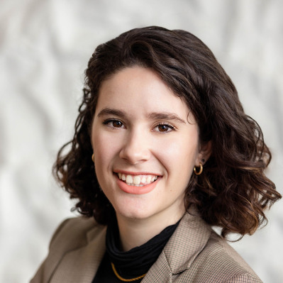 A Corporate headshot of a smiling white woman with short, curly brown hair, wearing gold earrings, a gold necklace, a taupe-colored blazer, and a black turtleneck.
http://www.annanproductions.com/