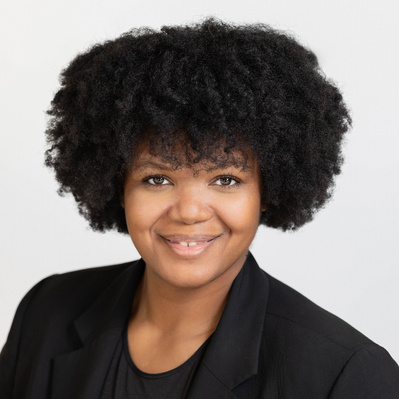 A Corporate headshot of a smiling black woman with short, natural, curly black hair, wearing a black blazer and a black inner shirt
http://www.annanproductions.com/