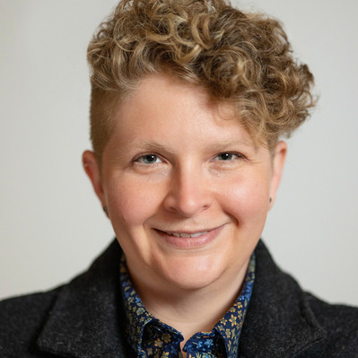 A Corporate headshot of a smiling white woman with short, curly blonde hair wearing a black wool blazer and a floral inner shirt
http://www.annanproductions.com/