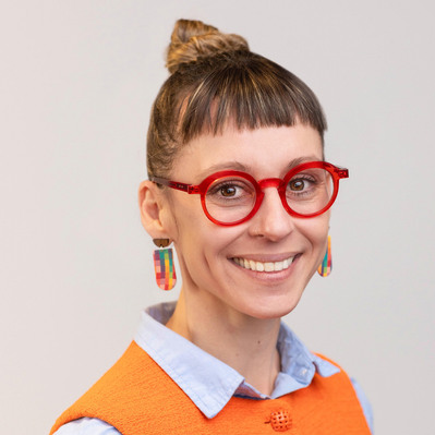 A Corporate headshot of a smiling white woman wearing colorful clay-made earrings, red glasses, baby blue long sleeves, and a bright orange vest at the Astho Conference 2023 in Crystal City, Virginia.
http://www.annanproductions.com/
