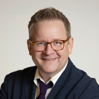A Corporate headshot of a smiling white man wearing brown glasses, a purple necktie, white inner shirt, and midnight blue gray sweater at the Astho Conference 2023 in Crystal City, Virginia.
http://www.annanproductions.com/