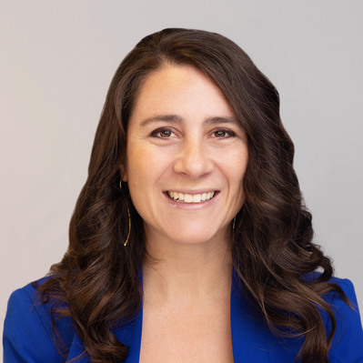 A corporate headshot of a smiling white woman with long, dark, loosely-curled brown hair, wearing gold earrings, a royal blue blazer, and a white inner garment top at the Astho Conference 2023 in Crystal City, Virginia.
http://www.annanproductions.com/