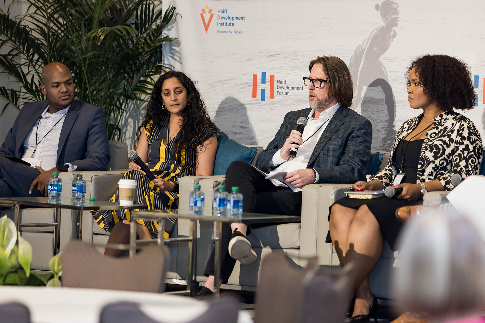 A four-speaker panel at the Haiti Development Forum consisted of a bald black man, an East Asian woman with curly black hair, a white man with glasses, and a black woman with short, tight curls.