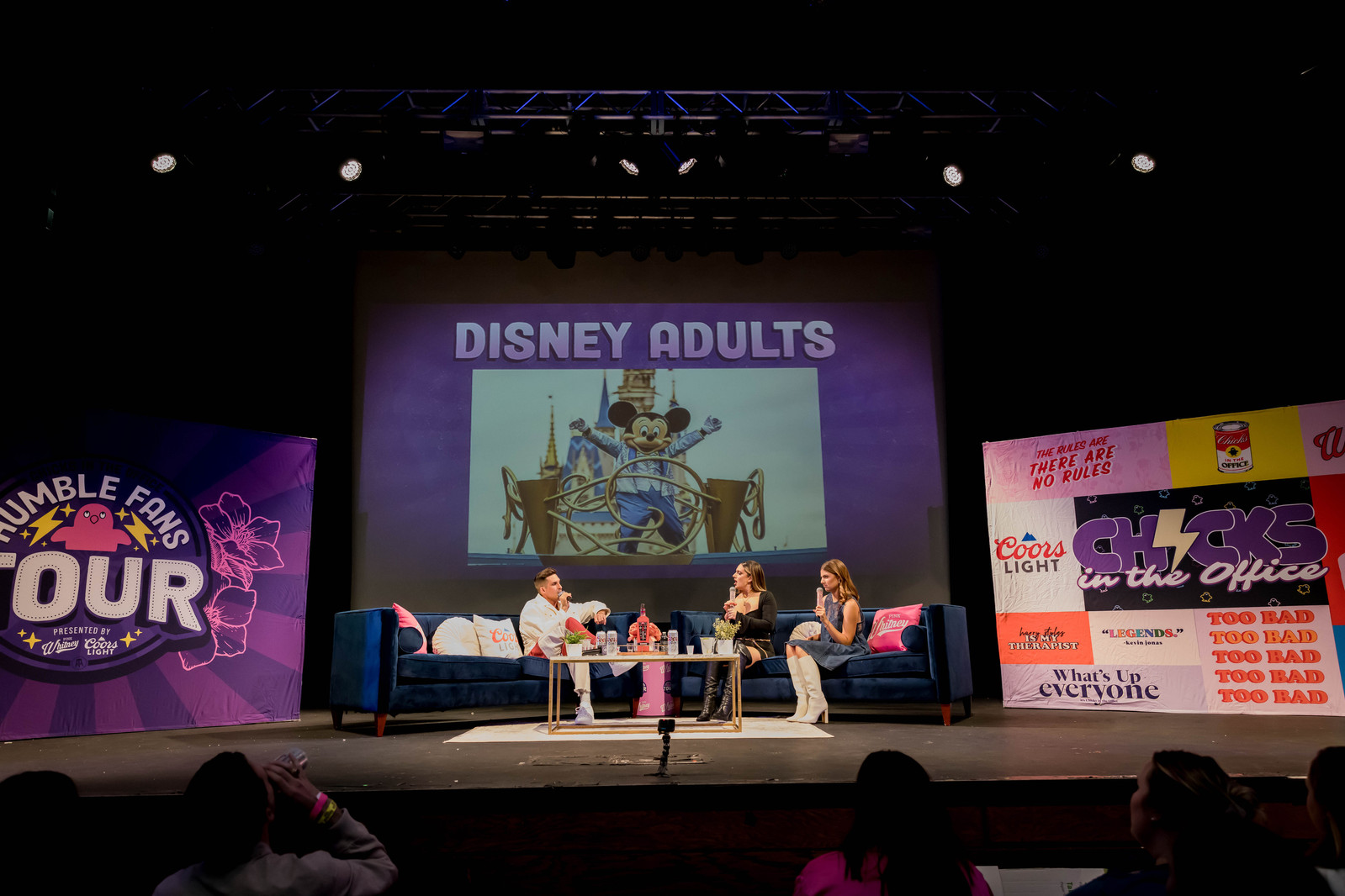 Two white female hosts with blonde hair interviewing a white man with blonde hair on a couch for the Disney Adults-Chicks in the Office Humble Fans Tour