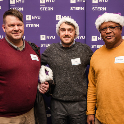 A white man wearing a red sweater and a backpack, a white man wearing a gray sweater and a Christmas hat, and a black man wearing a yellow sweater and a Christmas hat pose in front of a photo booth at a 2023 NYU Event.
http://www.annanproductions.com
