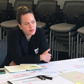 Hannah seated at a table listening to a user share feedback. Table has post its, books and papers.