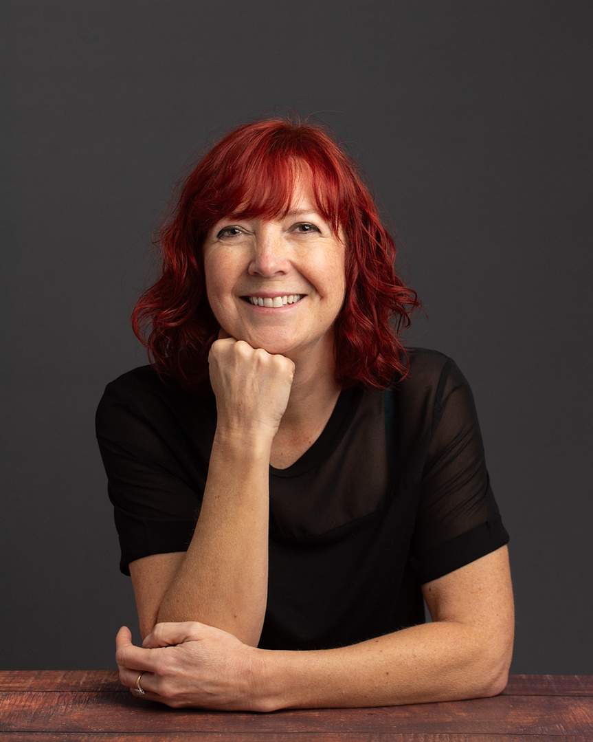 Female client with red hair and a black T-shirt top poses at a desk for a studio portair shoot