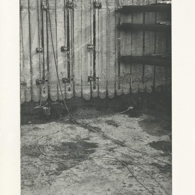 A deep construction excavation, with several corner braces off to the right side, and various pieces of debris in the mud at the bottom.