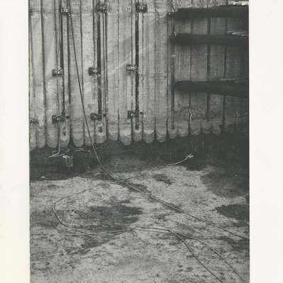 A deep construction excavation, with several corner braces off to the right side, and various pieces of debris in the mud at the bottom.