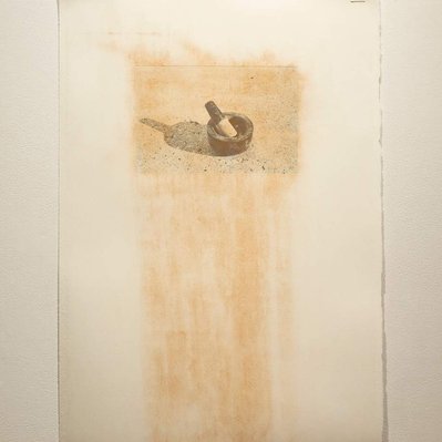 A photographic print of a mortar and pestle, on a large sheet of white paper. The paper is smeared with brick-red dust.