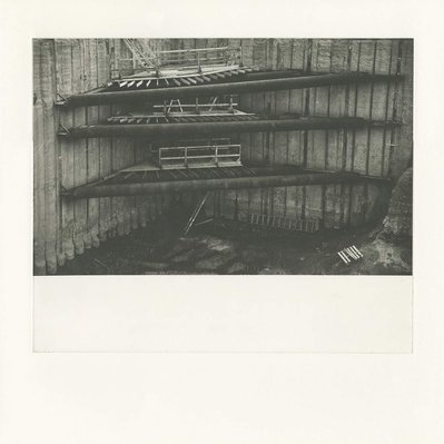 A deep construction excavation, with several corner braces In the centre. The top brace has begun to collapse, and the left end has fallen down. Wooden scaffolds with a stair and ladders run down just beyond the braces.