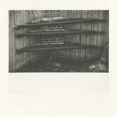 A deep construction excavation, with several corner braces In the centre. The top brace has begun to collapse, and the left end has fallen down. Wooden scaffolds with a stair and ladders run down just beyond the braces.