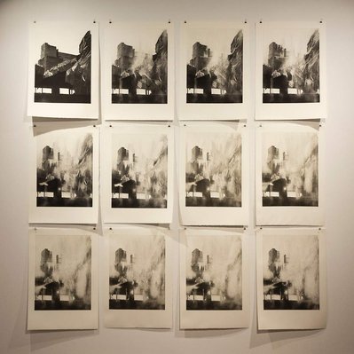12 prints on a white gallery wall. They all depict the same structure wrapped in tarps,  but in each print read left to right, top to bottom, the image becomes more and more worn away.