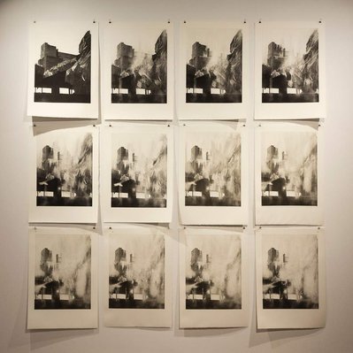 12 prints on a white gallery wall. They all depict the same structure wrapped in tarps,  but in each print read left to right, top to bottom, the image becomes more and more worn away.