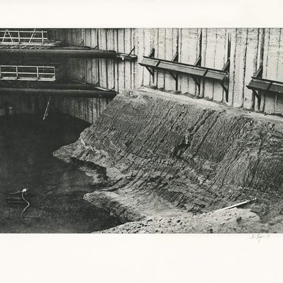 A bank of eroded soil and mud, against the wall of a construction excavation. A pump is barely visible in the standing water at the bottom of the bank.