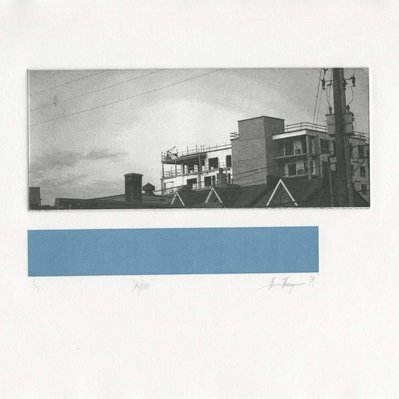 A photographic print of a distant condominium construction, in front of an expansive sky. Under the image, there is a blue rectangle.