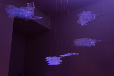 Several floating blocks of transparent sheets in various shapes, with engraved lines of maps and architectural plans on them. They are illuminated by a dramatic purple light.