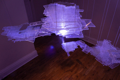 Several floating blocks of transparent sheets in various shapes, with engraved lines of maps and architectural plans on them. They are illuminated by a dramatic purple light.