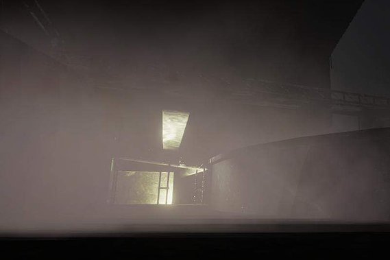 A computer-generated image of some large, low cylindrical structures emerging from darkness and mist, illuminated by a weak yellow light.
