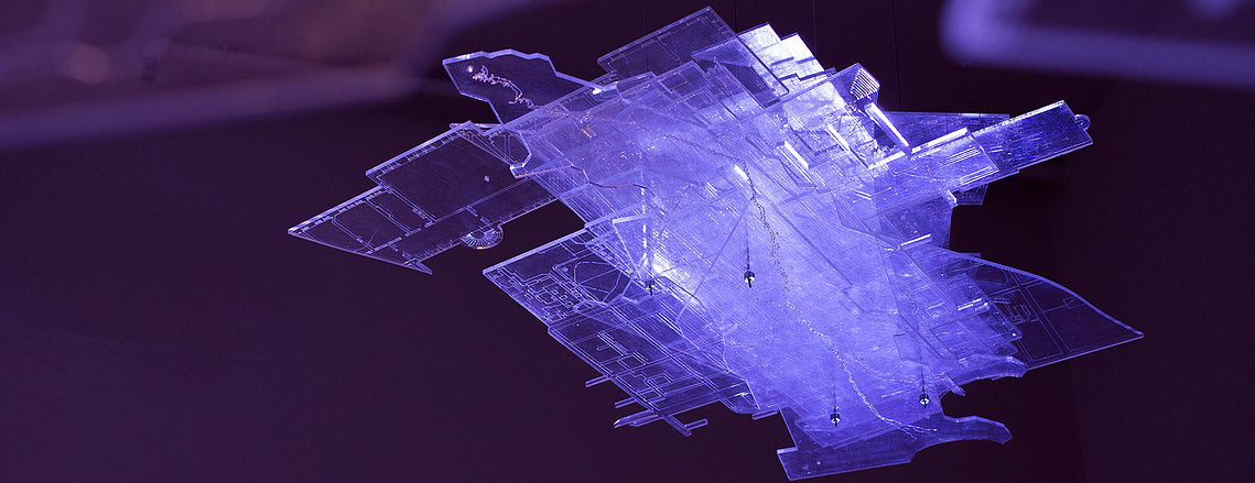 A floating block of transparent sheets in various shapes, with engraved lines of maps and architectural plans on them. They are illuminated by a dramatic purple light.