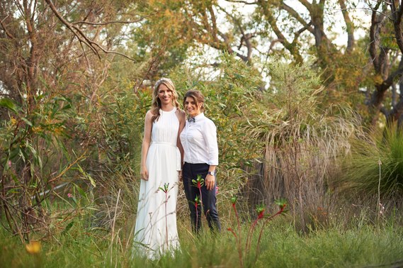 Two brides standing in a field, looking into the camera and smiling