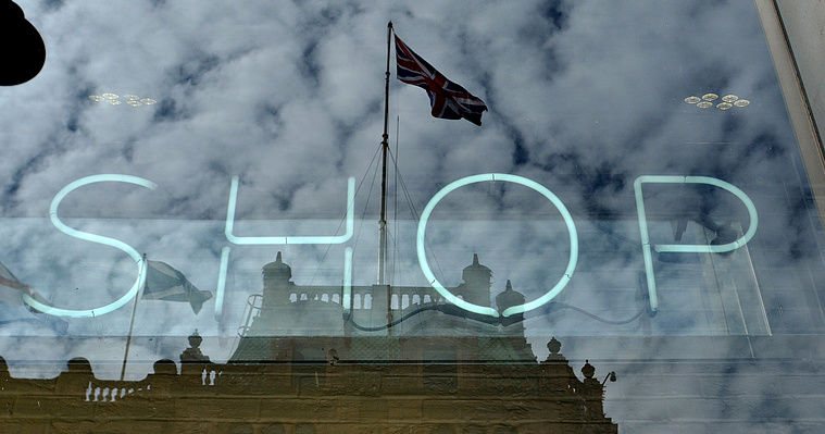 The word Shop seen through a glass shop window with Harrods reflected in the background