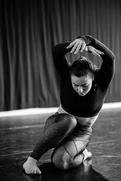 Young woman kneeling  and arms up in dance pose  with grace and effortlessness in soft light