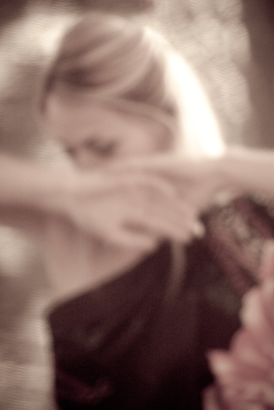 Blurry image of young woman with blond hair looking down and hands covering her face