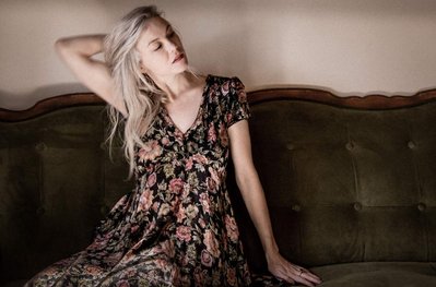 Young caucasian woman with silver hair & vintage floral dress sitting on vintage sofa