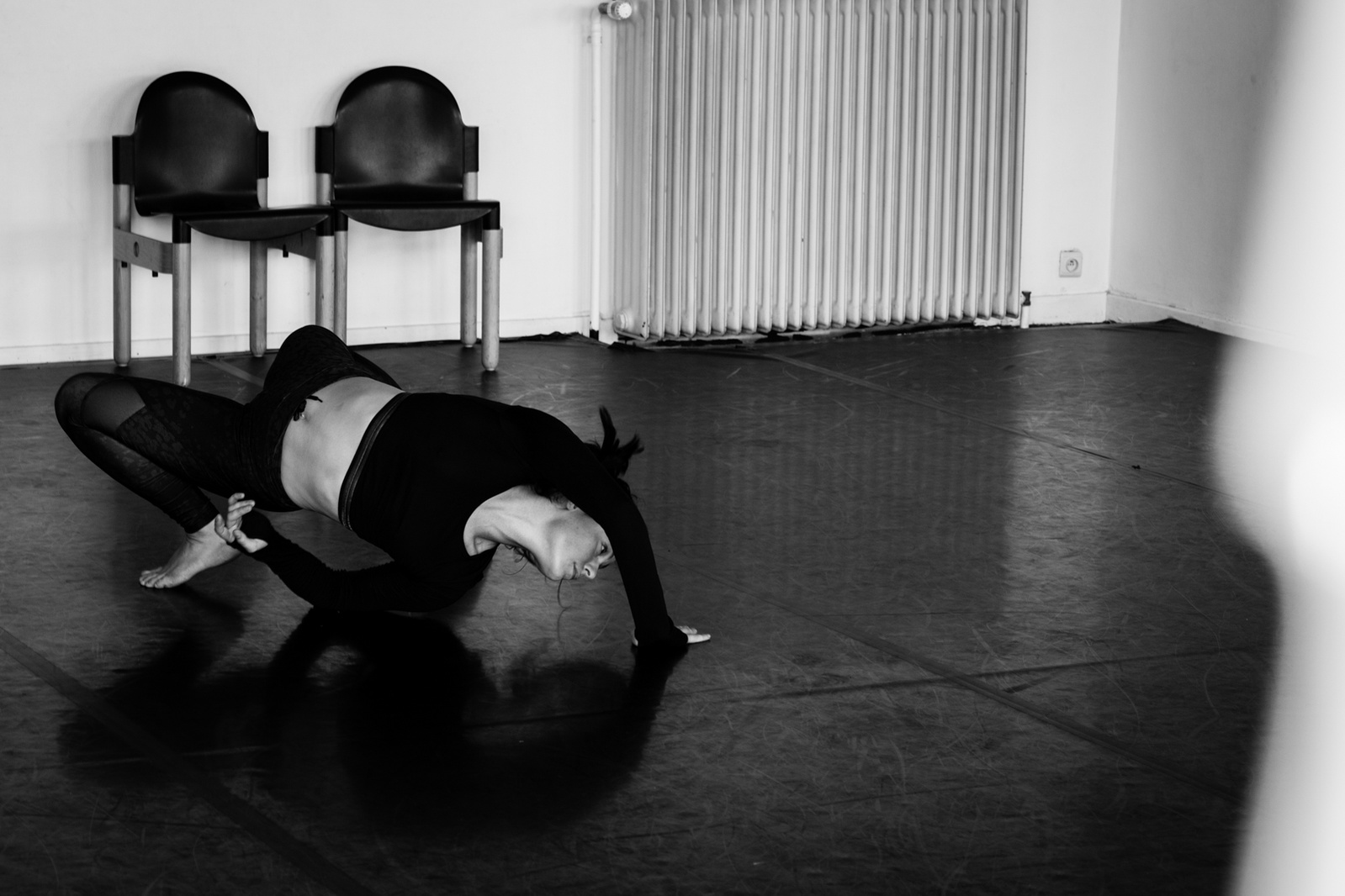 Young woman dancing, doing a back bend, in empty dance studio with two chairs behind her