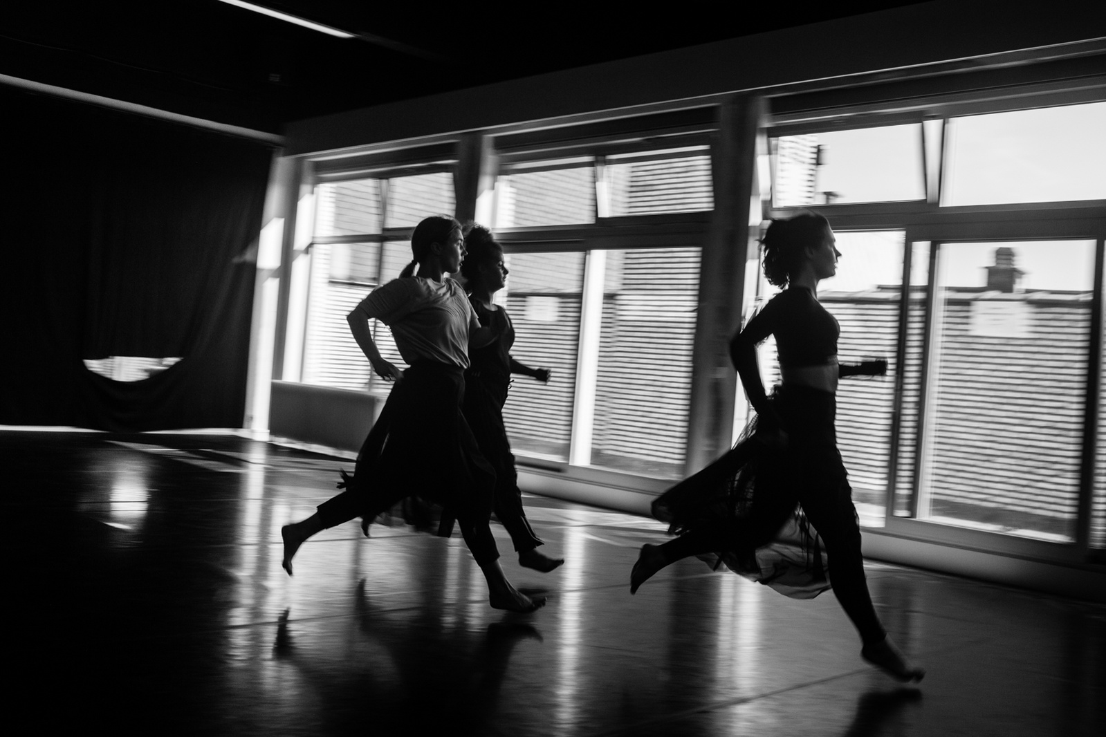Three young women in motion running in a dance studio with large window behind them