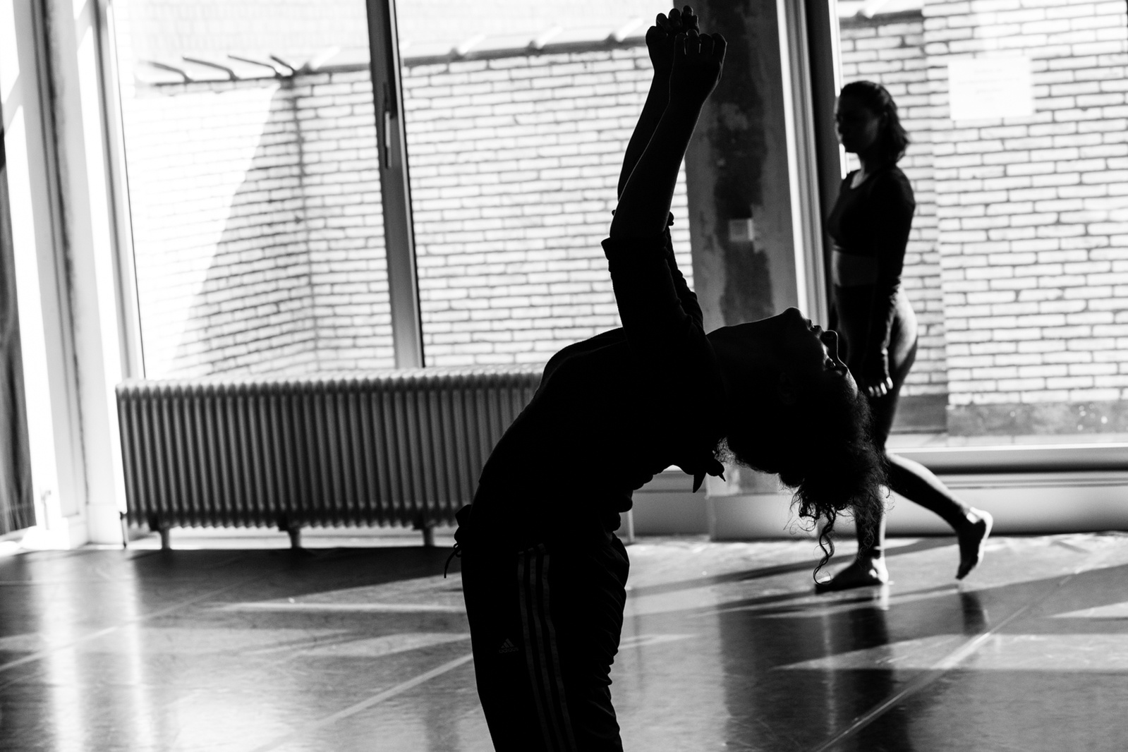 Silhouette of dancer bending backwards during dance routine with large window behind her