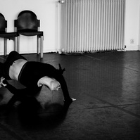 Young woman dancing, doing a back bend, in empty dance studio with two chairs behind her