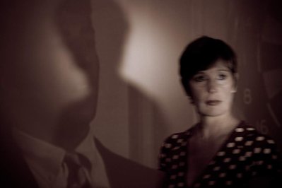 Woman with short hair and dramatic lighting gazes onwards as she moves by with her shadow behind her