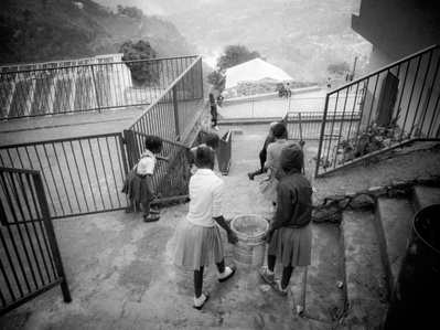 A scene taken from above of a group of Haitian children descending stairs carrying buckets of water