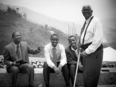 Four Haitian men laughing and conversing as they relax in rural background