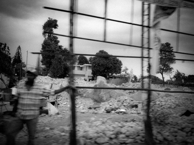 A man holds onto a structure in a pile of destruction on the streets of  Haiti