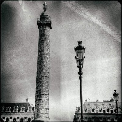 Black and white iPhone tintype of a statue of Napoleon in Paris and some older buildings in background from frog's perspective