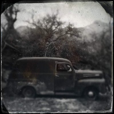 Black and white iPhone tintype of a vintage rusted, abandoned car in California desert set amongst trees