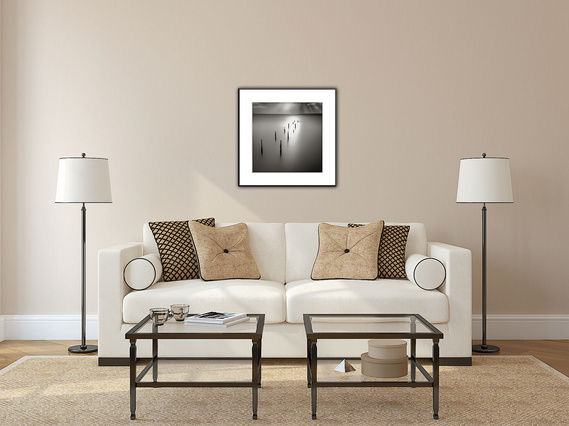 A simple black and white square framed photo of a ghost bird resting on a piling as sunrays gently bathe it fits the warm tones of this living area.